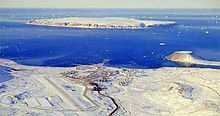 Aerial photograph of Thule Air Base with North Star Bay in the background. Land masses are show covered in snow, but the bay is not frozen over.